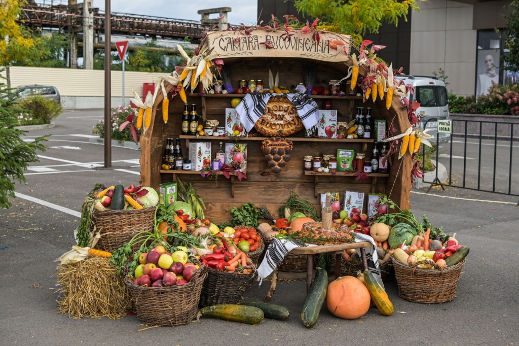 Stands cu produse tradiționale românești, inclusiv fructe, legume și conserve, decorat cu elemente autumnale.