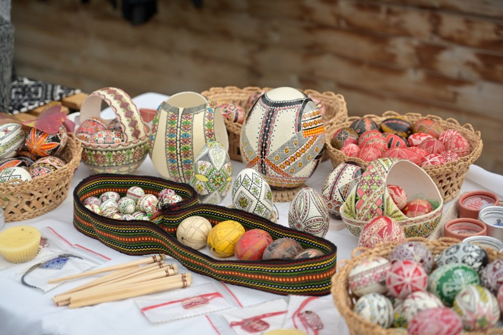 O masă plină cu ouă decorative colorate, tradiționale, expuse în coșuri din nuiele și pe o față de masă albă.