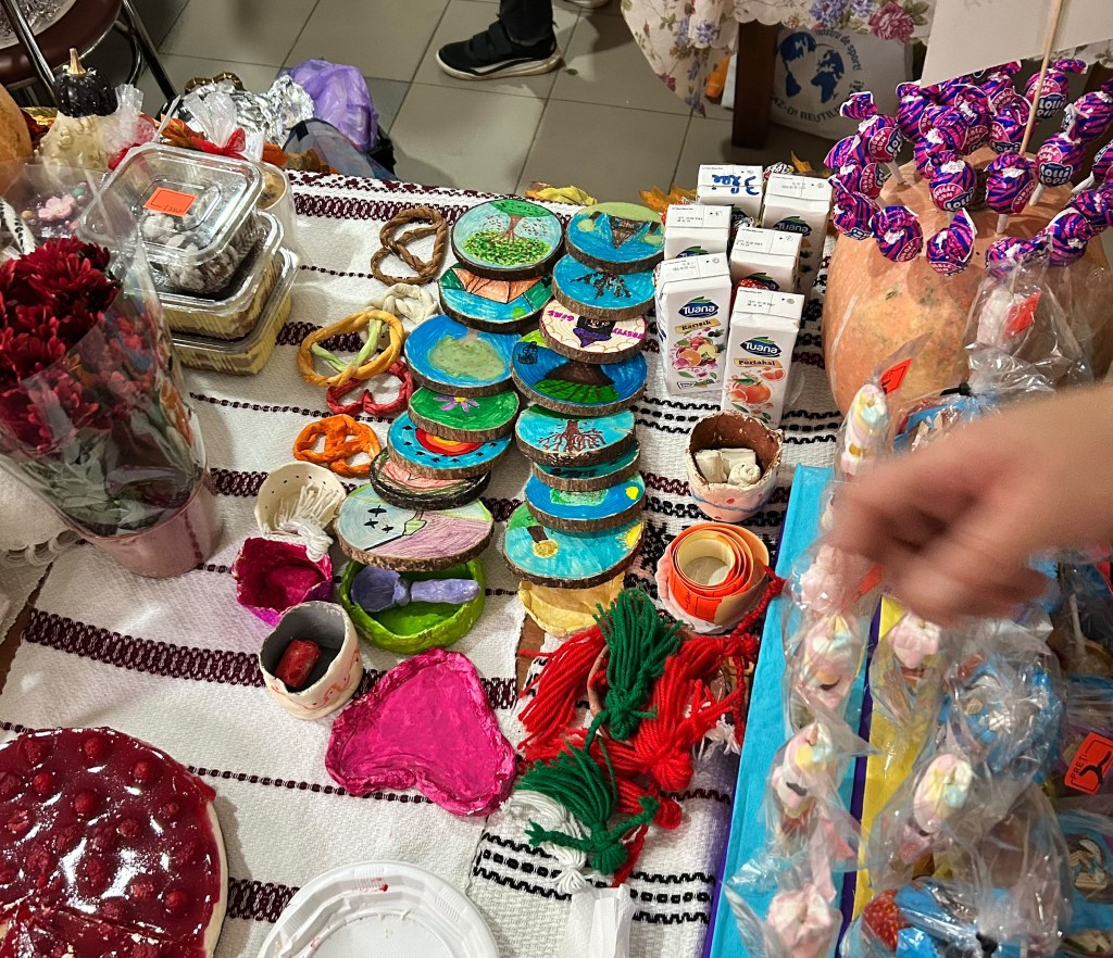 O varietate de obiecte artizanale și dulciuri, inclusiv pandantive pictate, florile de mătase, și batoane de nuntă, pe o masă decorată.