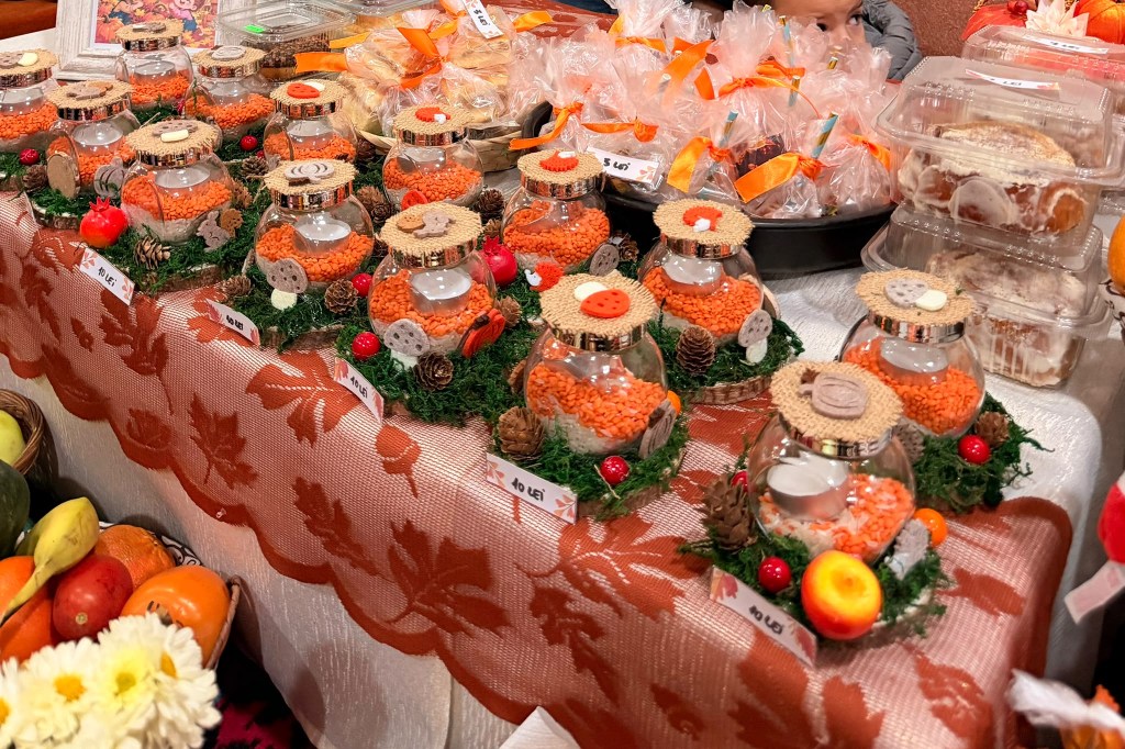 Masoniță cu decoruri colorate, pline cu boabe de diverse nuanțe, expuse pe o masă acoperită cu o față de masă elegantă, alături de produse de patiserie și fructe.